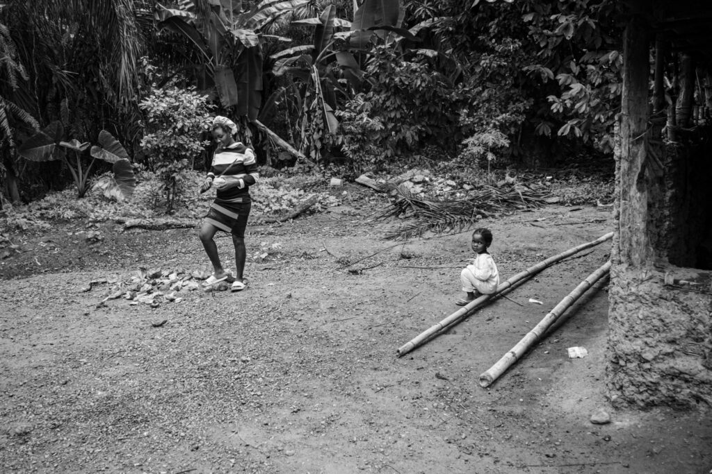A mother prepares coconuts beside her daughter at the forest edge in Massatin