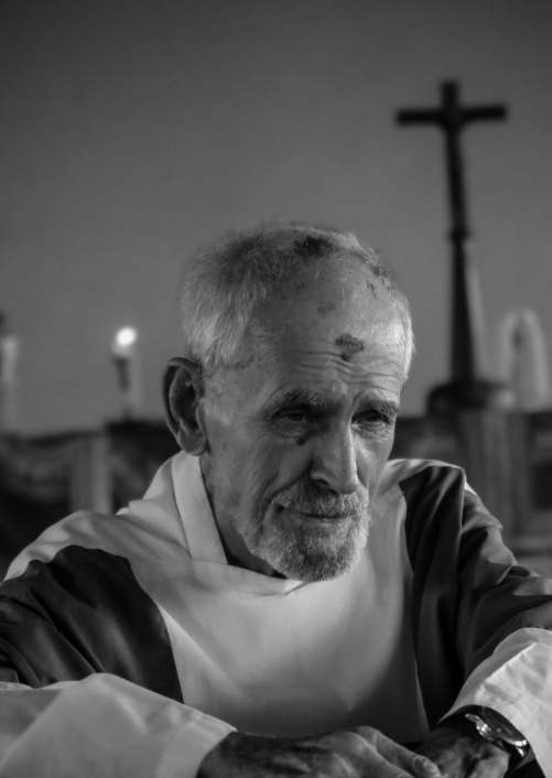 Portrait of Father Gareth Jenkins at dusk, a cross behind him
