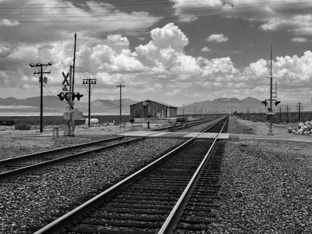 A railway crossing cuts through the landscape, its signals and tracks showing the practical infrastructure behind an apparently empty roadside scene.