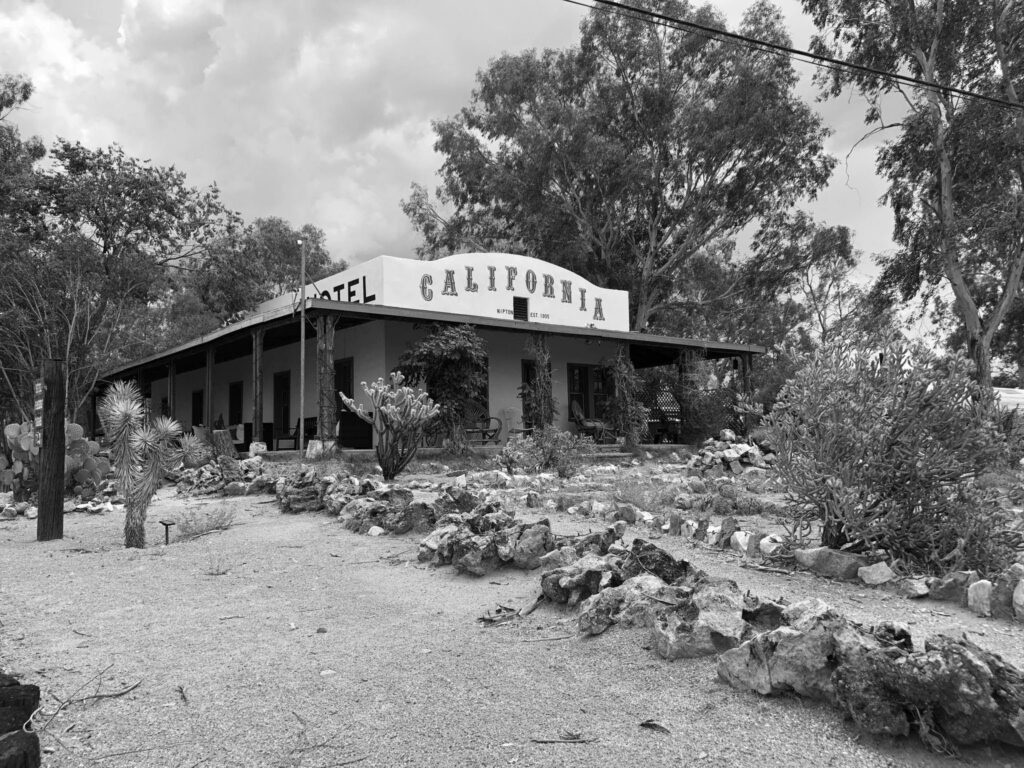 Hotel California in Nipton, California, sits among desert plants and rocks; its familiar name contrasts with the modest physical building.