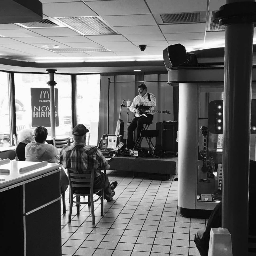 A guitarist performs on a small stage inside a McDonald’s restaurant in Tennessee while customers sit nearby, bringing a local moment into a globally recognisable setting.