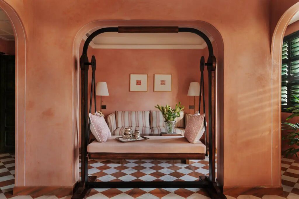 Pink lime-plastered suite with an arched opening and chequered floor at Abode Jaipur