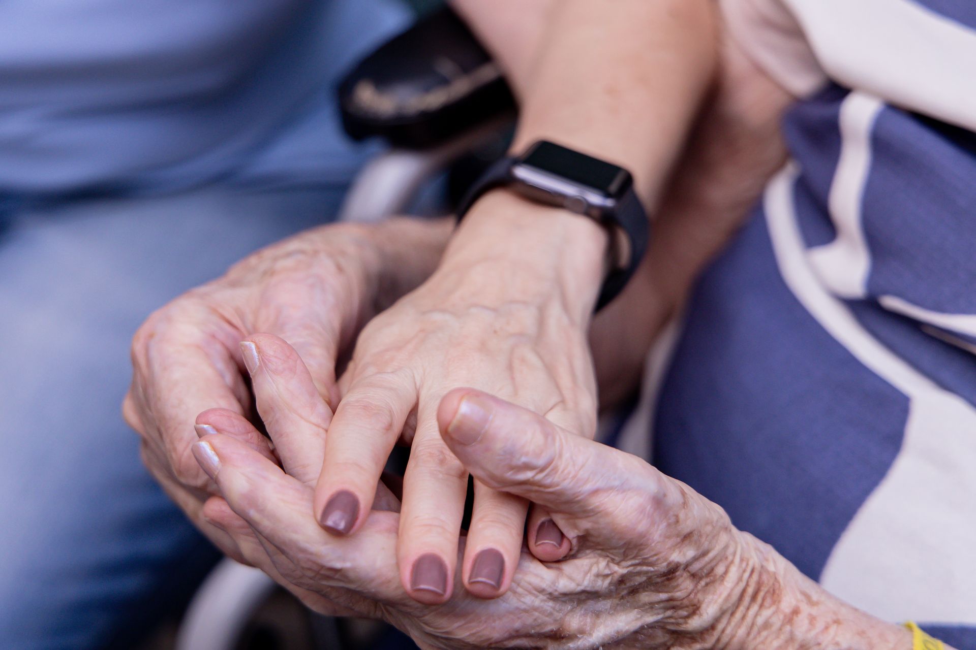A carer wearing a smartwatch holds an older person's hands, technology and care for an ageing population