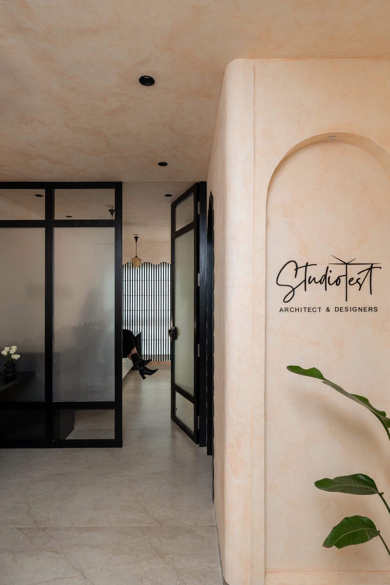Peach lime-washed studio with fluted glass partition and the Studio KNest wordmark