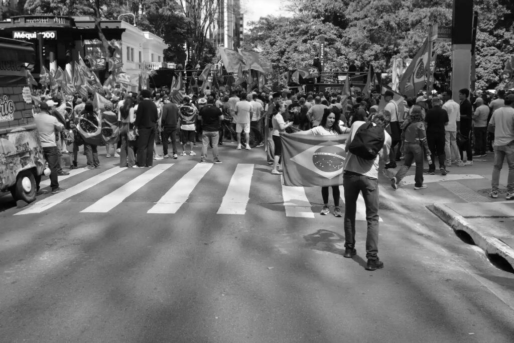 People occupy Avenida Paulista during a demonstration in support of Flávio Bolsonaro on 18 October 2026. The photograph establishes the public occasion around which the other pictures were made, before attention moves to the surrounding streets and individual encounters.