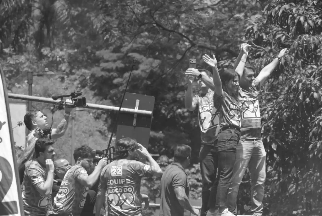Flávio Bolsonaro appears with other people on a raised platform at the demonstration. The photograph provides the political context for the series while remaining its only image centred on the rally platform.