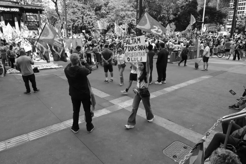 People, banners and campaign material share the space of the demonstration on Avenida Paulista. The photograph records the visible presence of supporters and observers within the gathering without attributing individual beliefs beyond what their actions show.