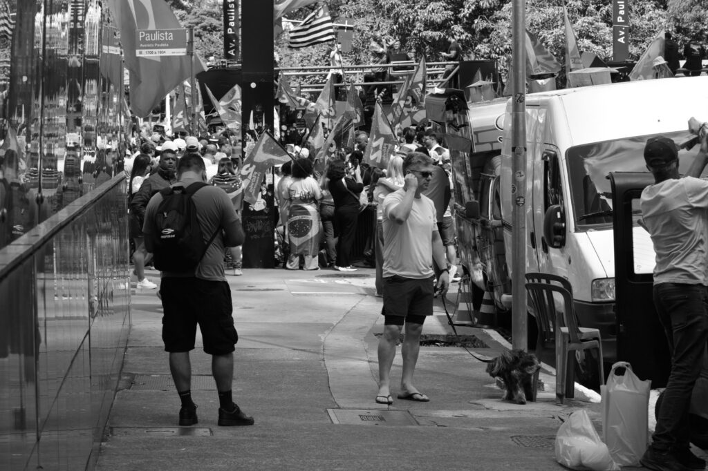 People pass through an area adjoining the demonstration. Their movement forms part of the street scene, although the photograph alone does not establish their reason for being there.