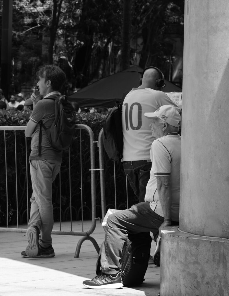 People stand or move near a column and a barrier beside the gathering. The photograph records the arrangement of bodies and street infrastructure through which people navigate the area.