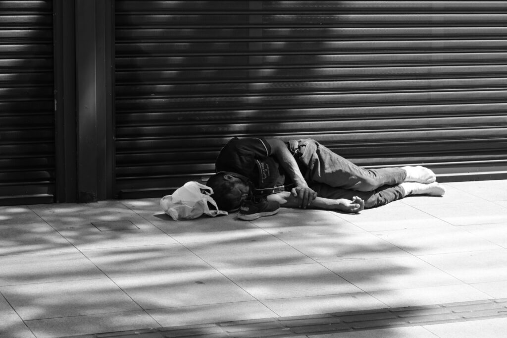 A person lies beside a metal shutter near the demonstration. The photograph records the visible posture and setting but does not establish the person's housing circumstances, health or relationship to the event.