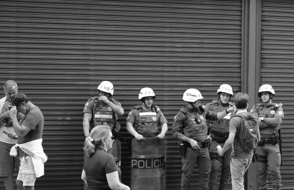 Police officers stand beside a shuttered building during the demonstration. The closed frontage and police presence show how the event intersects with ordinary commercial and pedestrian space.