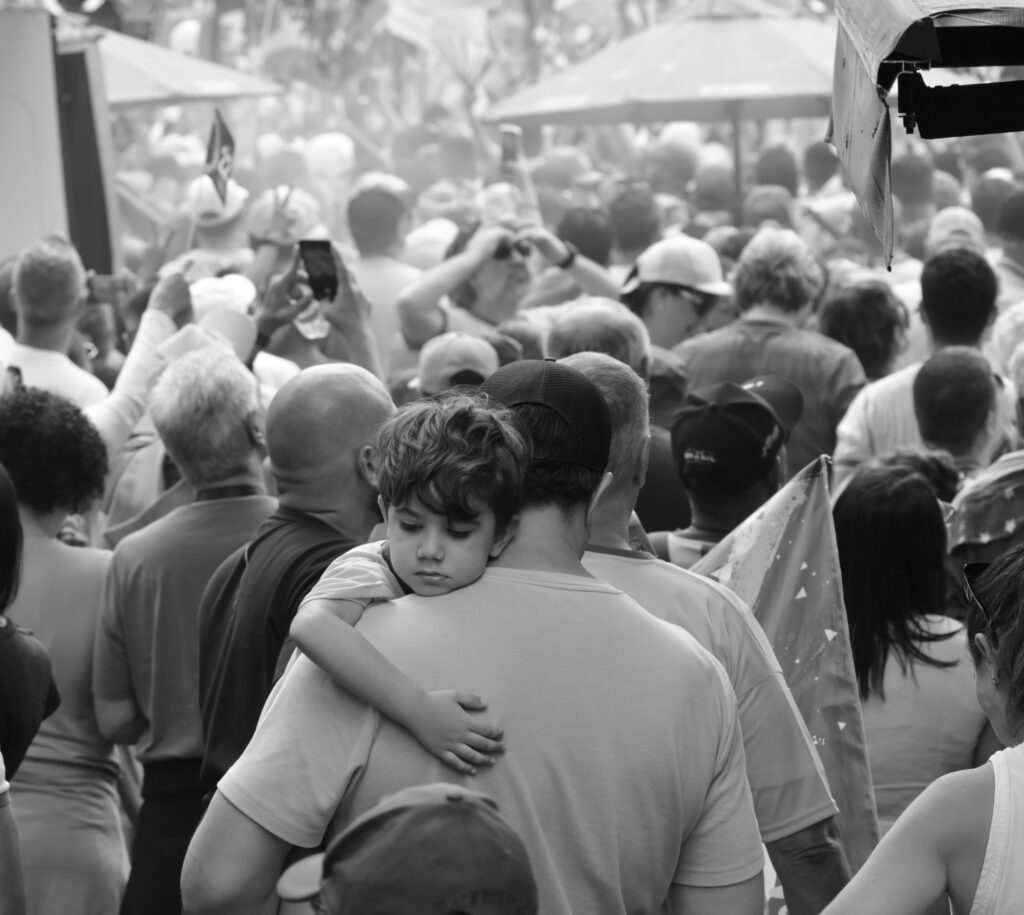 An adult holds a child close amid the people gathered on Avenida Paulista. The photograph records their proximity and the surrounding crowd without assigning political intentions to the child.