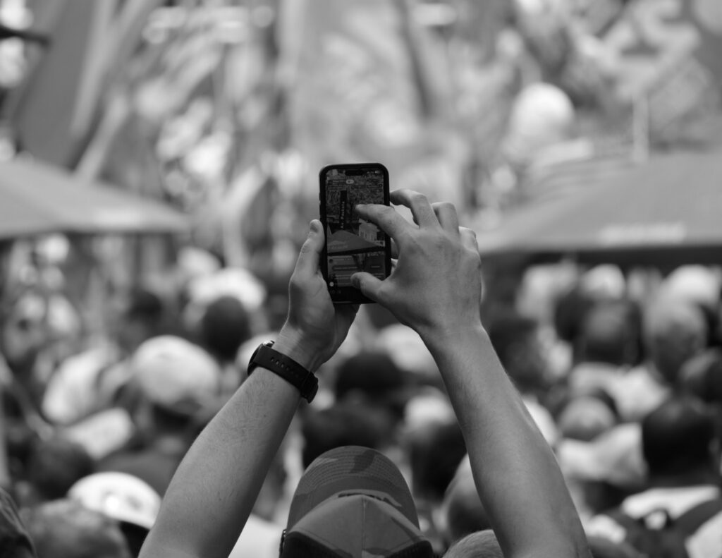 A person raises a mobile phone to record or photograph the demonstration. The gesture is another act of observation within the event and parallels the documentary photographer's own activity.