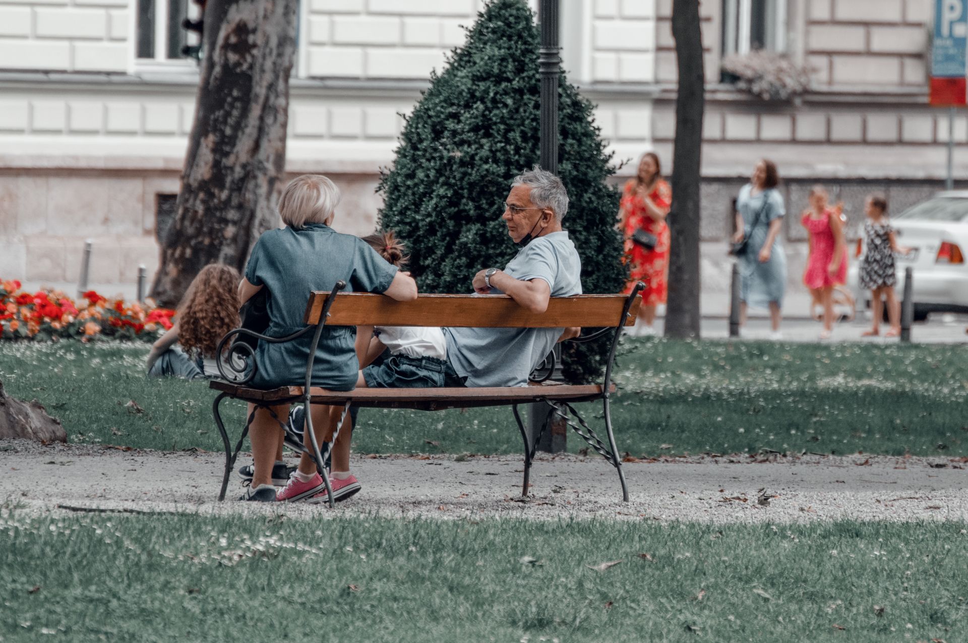 Two adults and a child talking on a wooden bench in a leafy city park