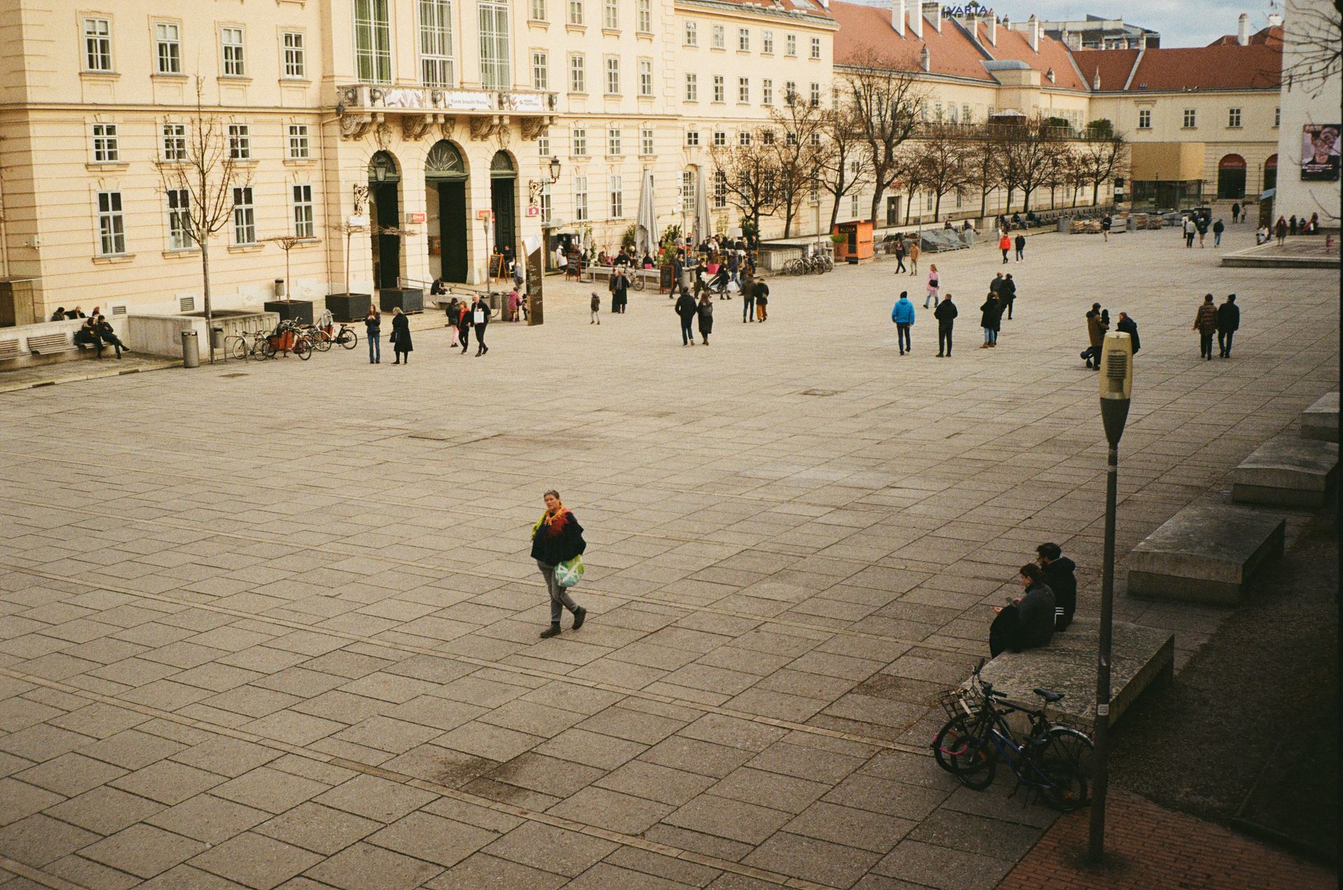 People walking across a wide paved town square lined with historic buildings