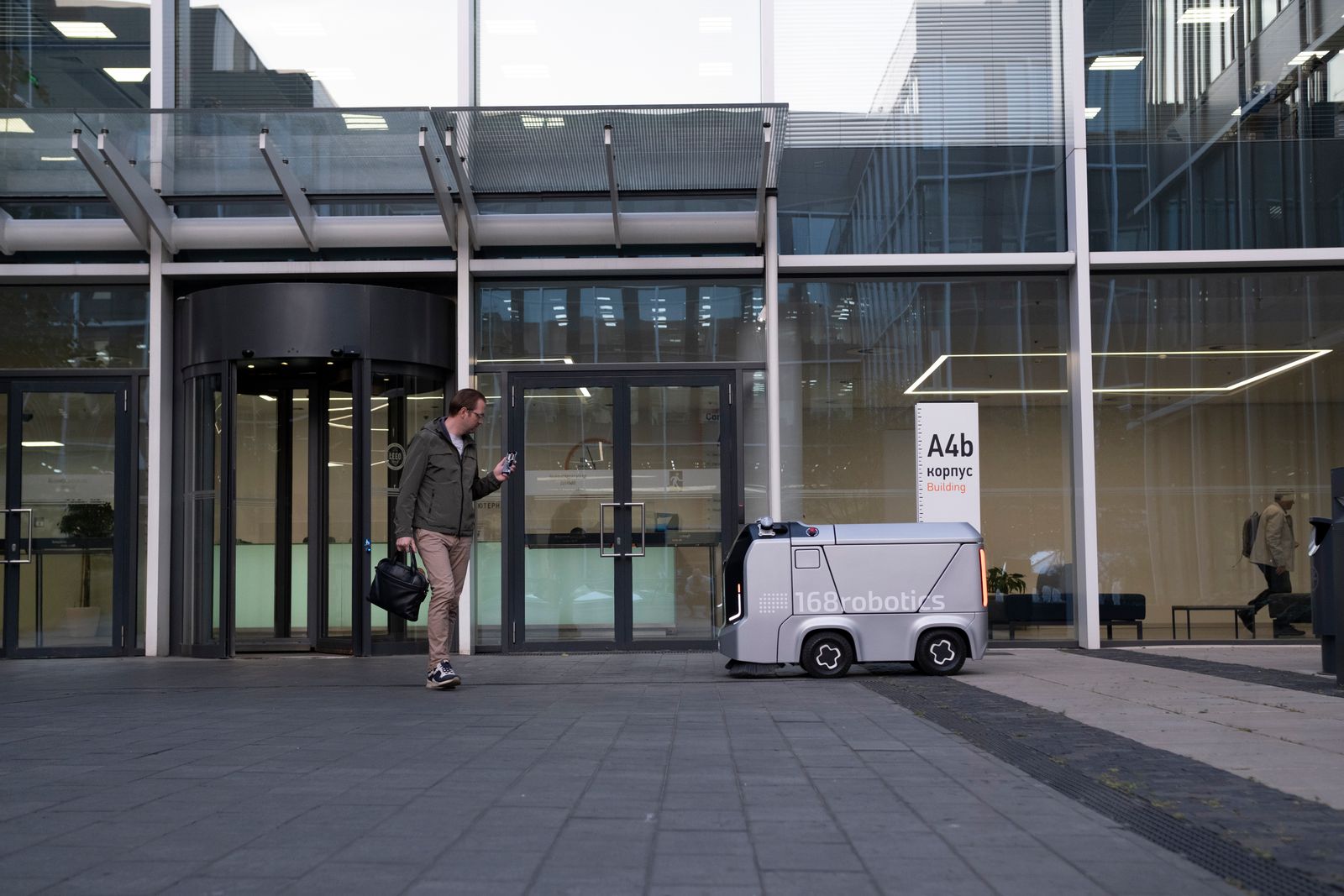 A man encounters an autonomous delivery robot outside a modern glass building